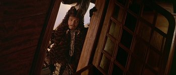 Movie still from “Pirates” (1986), directed by Roman Polanski – A man with long curly hair standing next to a door; Medium shot, Low angle