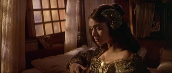 Movie still from “Pirates” (1986), directed by Roman Polanski – A woman in a gold dress is holding a pen; Close Up shot, Over the shoulder angle