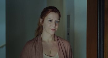 Movie still from “Pity” (2018), directed by Babis Makridis – A woman with red hair wearing a tan shirt and a pink sweater; Close Up shot, Over the shoulder angle
