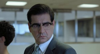 Movie still from “Pity” (2018), directed by Babis Makridis – A person wearing a suit and glasses; Close Up shot, Over the shoulder angle