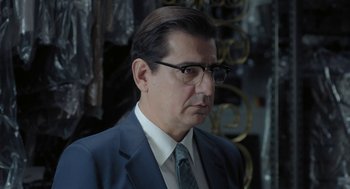 Movie still from “Pity” (2018), directed by Babis Makridis – A person wearing a suit and glasses; Close Up shot, Over the shoulder angle