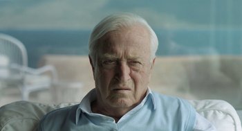 Movie still from “Pity” (2018), directed by Babis Makridis – An older man with a white hair and a blue shirt; Close Up shot, Over the shoulder angle
