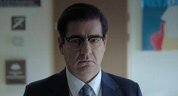 Movie still from “Pity” (2018), directed by Babis Makridis – A person wearing a suit and glasses; Close Up shot, Over the shoulder angle