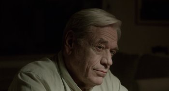 Movie still from “Pity” (2018), directed by Babis Makridis – An older man with white hair looking at the camera; Close Up shot, Over the shoulder angle