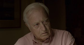 Movie still from “Pity” (2018), directed by Babis Makridis – An old man with white hair wearing a pink shirt; Close Up shot, Over the shoulder angle