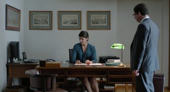 Movie still from “Pity” (2018), directed by Babis Makridis – A woman sitting at a desk in front of papers; Wide shot, High angle