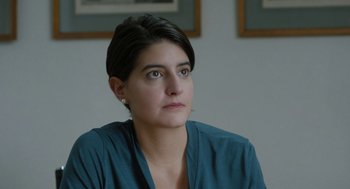 Movie still from “Pity” (2018), directed by Babis Makridis – A person sitting in a room; Close Up shot, Over the shoulder angle