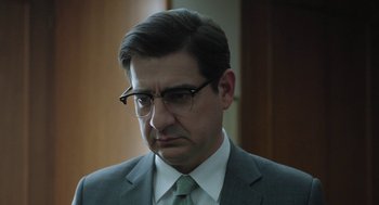 Movie still from “Pity” (2018), directed by Babis Makridis – A person wearing a suit and glasses; Close Up shot, Low angle