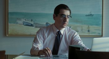 Movie still from “Pity” (2018), directed by Babis Makridis – A man sitting at a table looking at a computer screen; Medium shot, Low angle