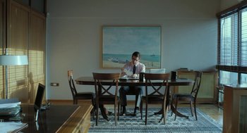Movie still from “Pity” (2018), directed by Babis Makridis – A man sitting at a dining room table; Wide shot, High angle