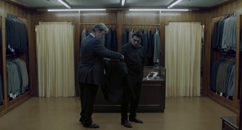 Movie still from “Pity” (2018), directed by Babis Makridis – Two men in a suit shop for suits in a suit shop; Medium shot, Over the shoulder angle