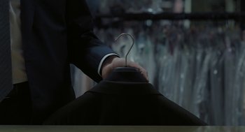 Movie still from “Pity” (2018), directed by Babis Makridis – A man in a suit and tie holding a hanger; Medium shot, High angle