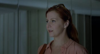 Movie still from “Pity” (2018), directed by Babis Makridis – A person wearing glasses and a pink shirt; Close Up shot, Over the shoulder angle