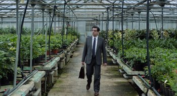 Movie still from “Pity” (2018), directed by Babis Makridis – A man in a suit and tie walking through a greenhouse; Medium shot, Low angle