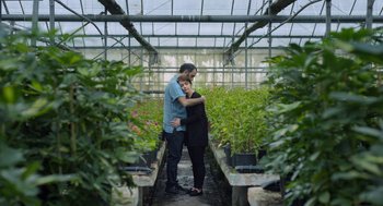 Movie still from “Pity” (2018), directed by Babis Makridis – A man and a woman hugging in a greenhouse; Medium shot, High angle