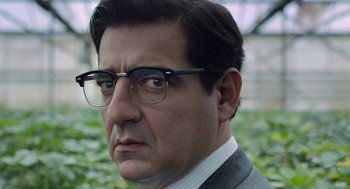 Movie still from “Pity” (2018), directed by Babis Makridis – A person wearing glasses and a suit; Close Up shot, Over the shoulder angle