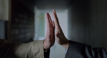 Movie still from “Pity” (2018), directed by Babis Makridis – Two people giving a high five in front of a window; Extreme Close Up shot, Low angle