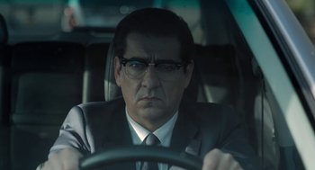Movie still from “Pity” (2018), directed by Babis Makridis – A man in a suit and glasses driving a car; Close Up shot, Over the shoulder angle