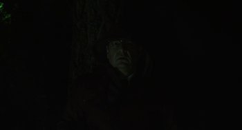 Movie still from “Pity” (2018), directed by Babis Makridis – A man wearing a hat and a coat is in the dark; Medium shot, Low angle