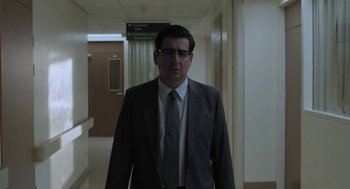 Movie still from “Pity” (2018), directed by Babis Makridis – A man in a suit and tie standing in a hospital hallway; Medium shot, Low angle