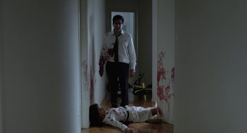 Movie still from “Pity” (2018), directed by Babis Makridis – A man standing next to a dead body covered in blood; Wide shot, Low angle