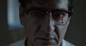 Movie still from “Pity” (2018), directed by Babis Makridis – A person wearing glasses with blood on his face; Close Up shot, Low angle