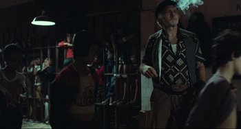 Movie still from “Pixote” (1980), directed by Hector Babenco – A man smoking a cigarette in front of a group of people; Medium shot, Over the shoulder angle