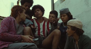 Movie still from “Pixote” (1980), directed by Hector Babenco – A group of young men sitting next to each other on the ground; Medium shot, Low angle