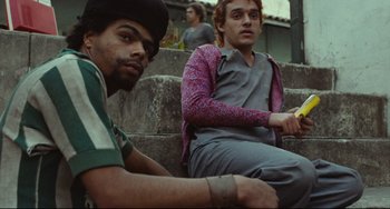 Movie still from “Pixote” (1980), directed by Hector Babenco – Two young men sitting on steps holding a cell phone; Medium shot, Low angle