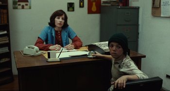 Movie still from “Pixote” (1980), directed by Hector Babenco – Two people sitting at a desk in a room; Medium shot, Over the shoulder angle