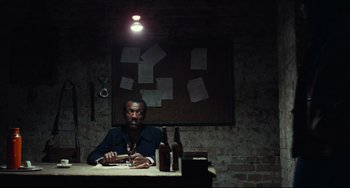 Movie still from “Pixote” (1980), directed by Hector Babenco – A man sitting at a table in a dark room; Medium shot, High angle