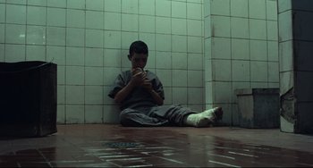 Movie still from “Pixote” (1980), directed by Hector Babenco – A man sitting on the ground holding a cell phone; Wide shot, High angle