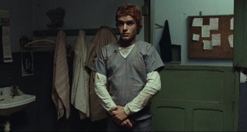 Movie still from “Pixote” (1980), directed by Hector Babenco – A man in a hospital gown standing in a room with his hands crossed; Medium shot, Low angle