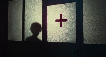 Movie still from “Pixote” (1980), directed by Hector Babenco – A shadow of a person standing in front of a window with a cross on it; Medium shot, Low angle