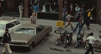 Movie still from “Pixote” (1980), directed by Hector Babenco – A group of people standing on a sidewalk next to parked motorcycles; Wide shot, High angle