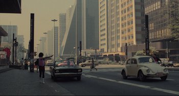Movie still from “Pixote” (1980), directed by Hector Babenco – A car driving down a street past tall buildings in a city; Extreme Wide shot, High angle