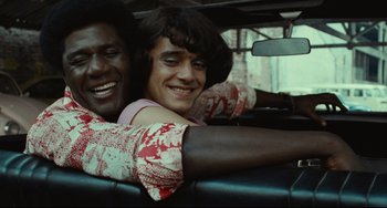 Movie still from “Pixote” (1980), directed by Hector Babenco – Two people in the back seat of a car smiling; Close Up shot, High angle