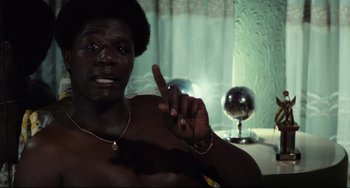 Movie still from “Pixote” (1980), directed by Hector Babenco – A man with a beard and a necklace is holding his finger up; Medium shot, Low angle