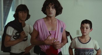 Movie still from “Pixote” (1980), directed by Hector Babenco – A man in a pink shirt is smoking a cigarette; Medium shot, Over the shoulder angle