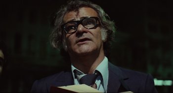 Movie still from “Pixote” (1980), directed by Hector Babenco – A man in a suit and tie holding an open book; Close Up shot, Low angle