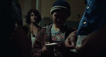 Movie still from “Pixote” (1980), directed by Hector Babenco – A young boy holding a cell phone while standing next to a woman; Close Up shot, Over the shoulder angle