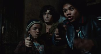 Movie still from “Pixote” (1980), directed by Hector Babenco – A group of young men holding guns in a dark room; Medium shot, Low angle