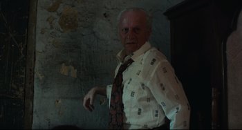 Movie still from “Pixote” (1980), directed by Hector Babenco – An older man wearing a tie in a room with peeling walls; Medium shot, Low angle