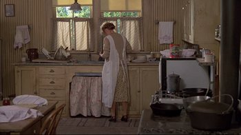 Movie still from “Places in the Heart” (1984), directed by Robert Benton – A woman standing in a kitchen preparing a meal; Wide shot, High angle