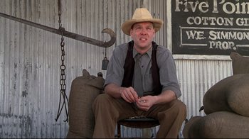 Movie still from “Places in the Heart” (1984), directed by Robert Benton – A man sitting on top of a chair wearing a hat; Medium shot, Low angle