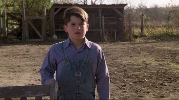 Movie still from “Places in the Heart” (1984), directed by Robert Benton – A young boy in overalls standing in front of a barn; Medium shot, High angle