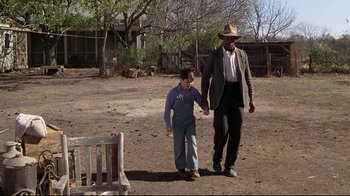 Movie still from “Places in the Heart” (1984), directed by Robert Benton – A man and a boy holding hands while walking in the dirt; Wide shot, Over the shoulder angle