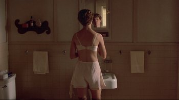 Movie still from “Places in the Heart” (1984), directed by Robert Benton – A woman in a white bathing suit looking in the mirror; Medium shot, Over the shoulder angle