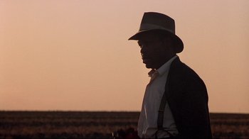 Movie still from “Places in the Heart” (1984), directed by Robert Benton – A man in a hat and a suit standing in a field at sunset; Close Up shot, Low angle