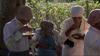 Movie still from “Places in the Heart” (1984), directed by Robert Benton – A group of people standing next to each other eating food; Medium shot, High angle